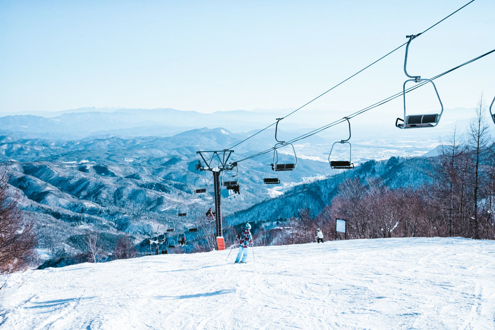 雪に覆われたゲレンデを滑るスキーヤーとリフトがある雪山の風景