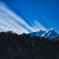 雪化粧した冬山から続く白い巻雲と青空の山岳風景の写真