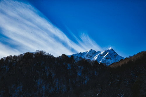 雪化粧した冬山から続く白い巻雲と青空の山岳風景