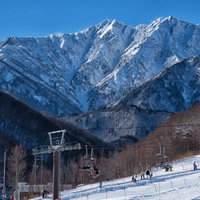 スキー場のゲレンデとリフト越しに見える雪化粧の爺ヶ岳（北アルプス）の写真