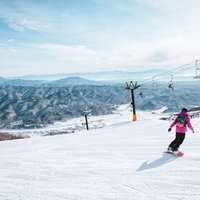 ゲレンデを滑るスノーボーダーとリフトが見える雪山の写真