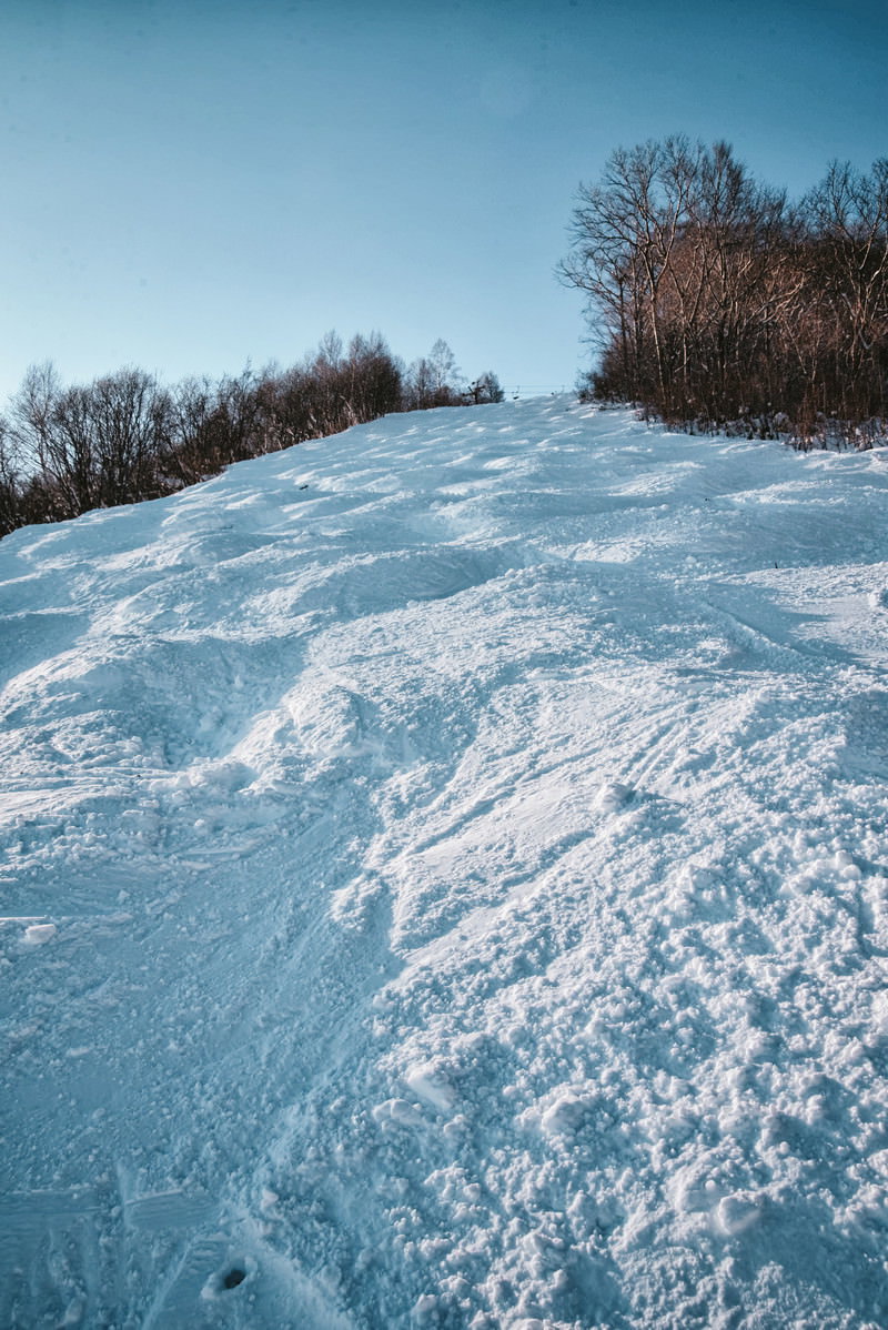 青空の下、起伏のあるスキーコースに雪が積もったゲレンデの風景