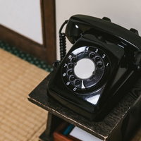 和室の畳の片隅に置かれた黒いダイヤル式電話の写真