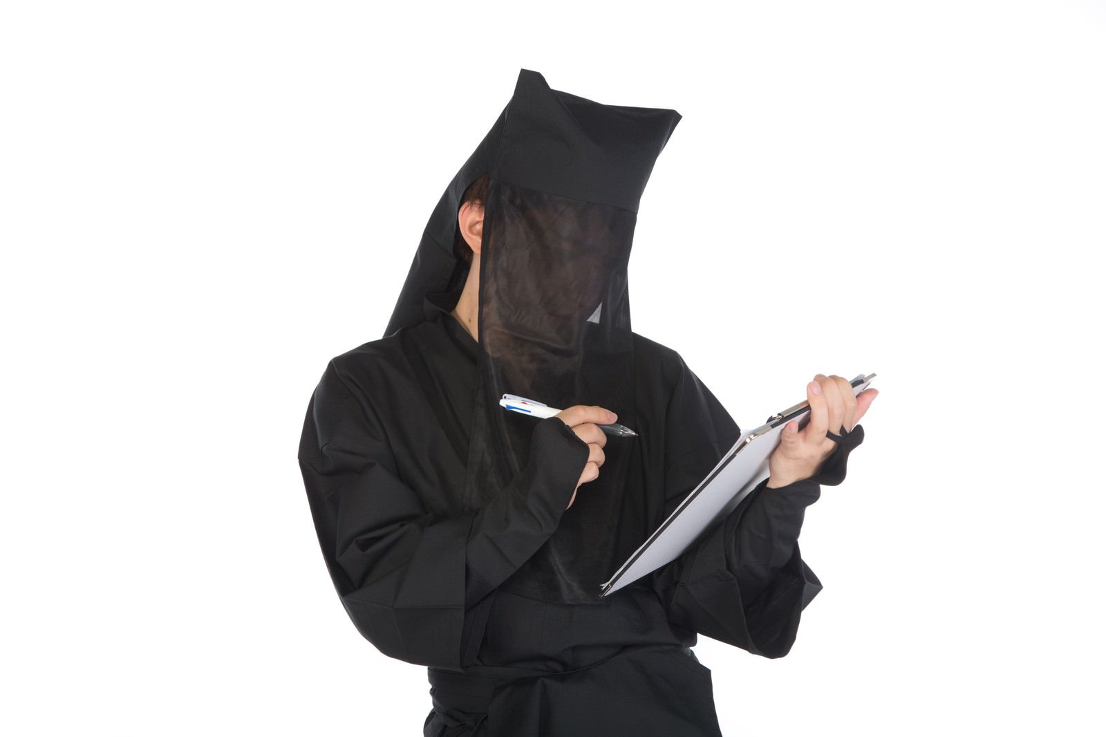 黒い頭巾で顔を覆った人物がアンケート用紙を持ち、ペンで記入している［モデル：鈴木秀］