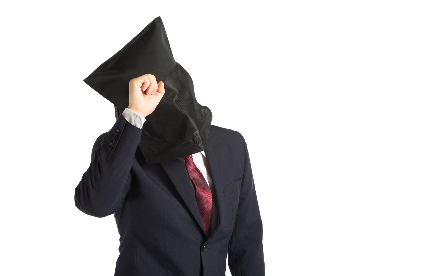 黒いフードで顔を隠し、拳を顔に当てるポーズを取る紺スーツの会社員［モデル：鈴木秀］