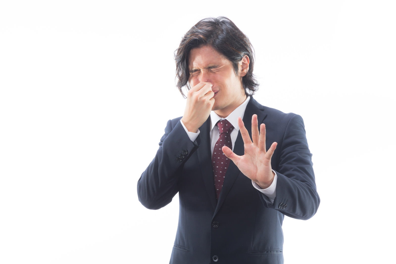 鼻をつまんで顔をゆがめ停止ポーズをするスーツの男性［モデル：竹田匡宏］