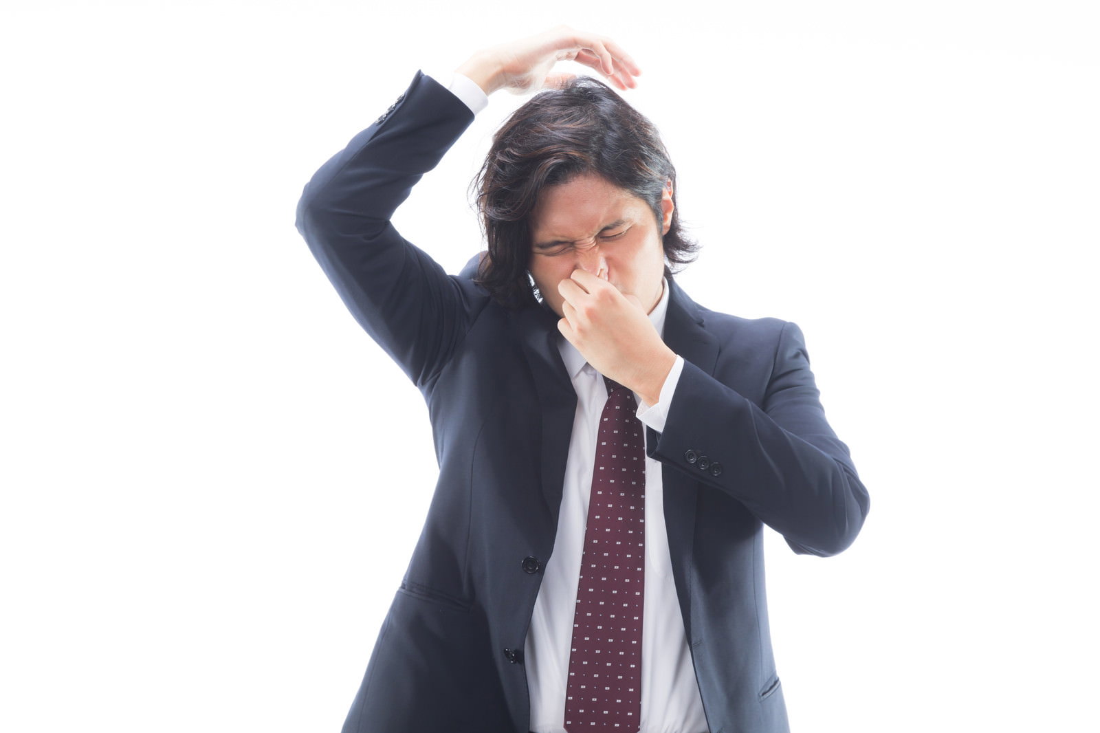 脇のにおいに困って頭を抱え鼻を押さえるスーツ姿の男性会社員［モデル：竹田匡宏］
