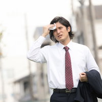 暑い外回りで額の汗を拭う飛び込み営業マンの写真
