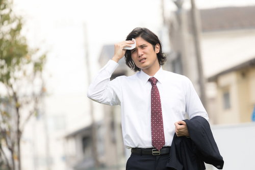 暑い外回りで額の汗を拭う飛び込み営業マン