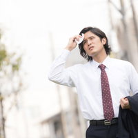 暑くて上着を脱ぐサラリーマン（営業中の外回り）の写真