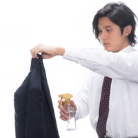 黒いスーツの上着に消臭スプレーをかける会社員の写真