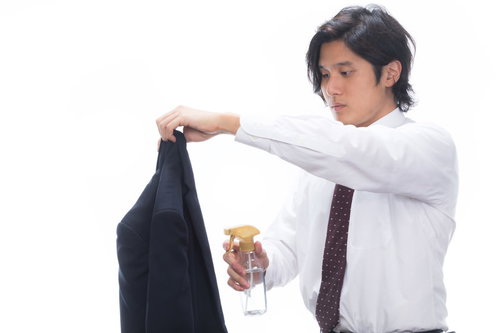 黒いスーツの上着に消臭スプレーをかける会社員