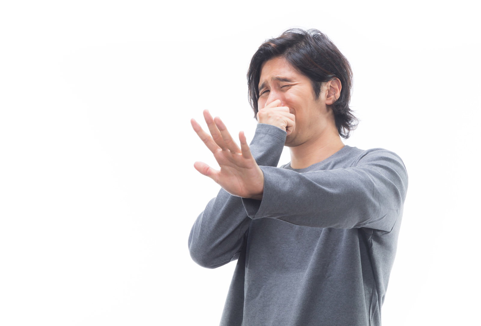 グレーのシャツを着た男性が鼻を押さえながら、片手を前に突き出して拒否する姿勢［モデル：竹田匡宏］