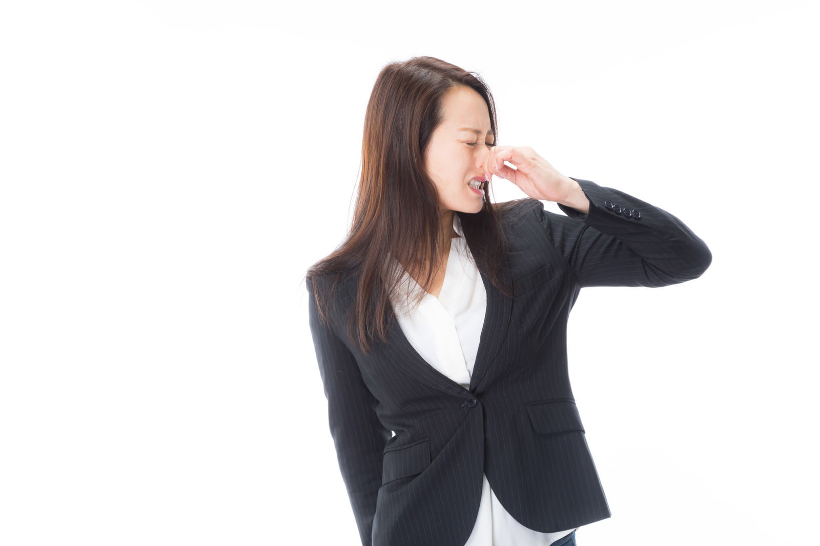 黒いスーツを着た女性が鼻をつまんで顔を背けている様子［モデル：土本寛子］