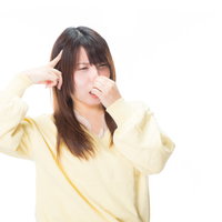 悪臭で頭痛がひどい黄色いトップスの女性が頭を抱えるの写真
