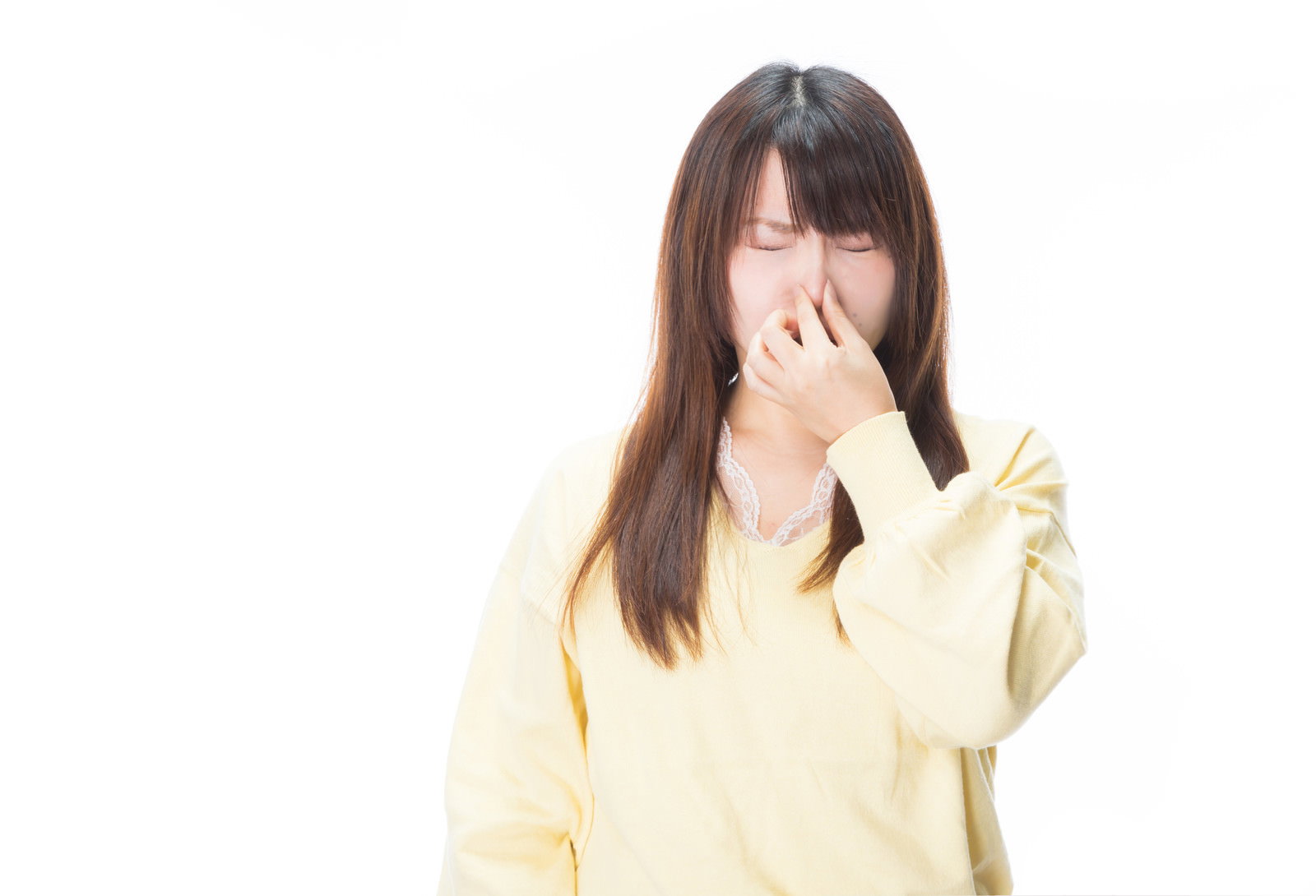 鼻をつまんで嫌そうな表情を浮かべる黄色いセーターの女性［モデル：Lala］