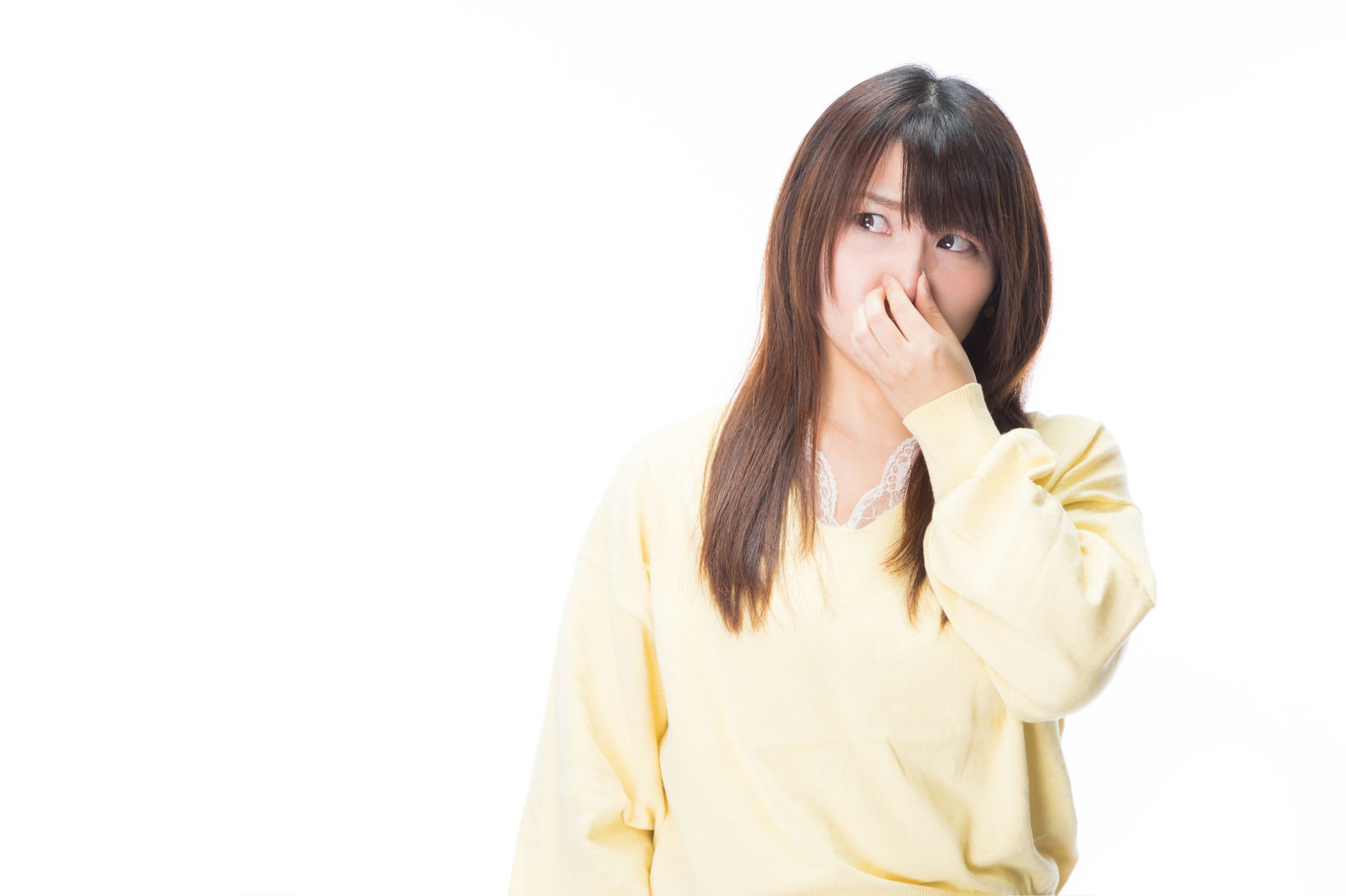 黄色いセーターを着た女性が手で鼻をつまんで不快そうな表情をしている［モデル：Lala］