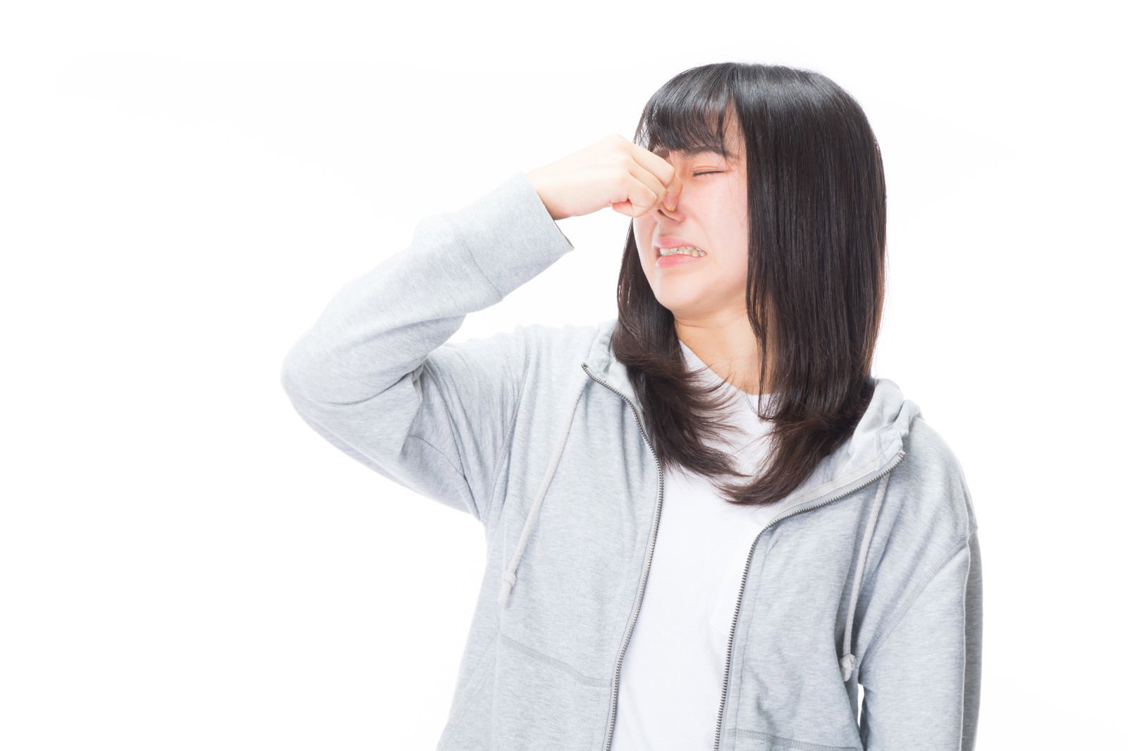 グレーのパーカーを着た女性が鼻をつまんで嫌がる表情をしている［モデル：Mizuho］