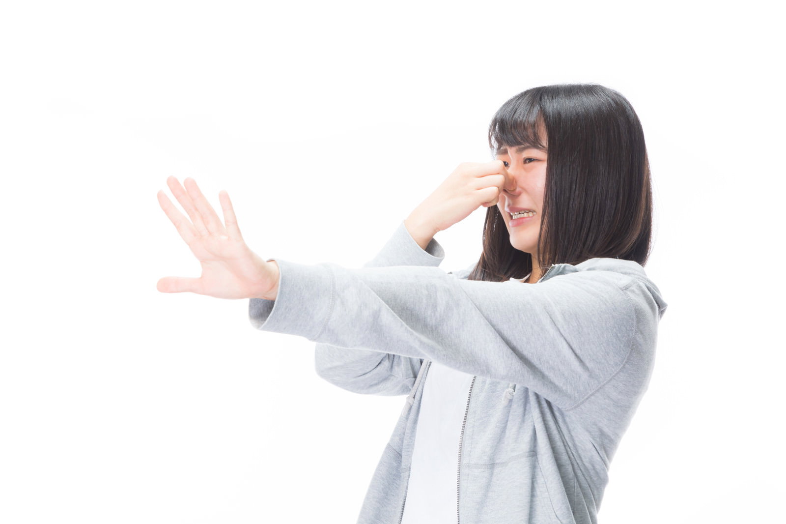 グレーのパーカーを着た女性が鼻をつまみながら片手を前に突き出している［モデル：Mizuho］