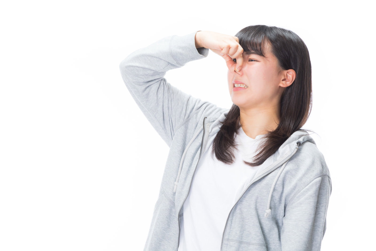 グレーのパーカーを着た女性が鼻をつまんで顔を歪めている様子［モデル：Mizuho］