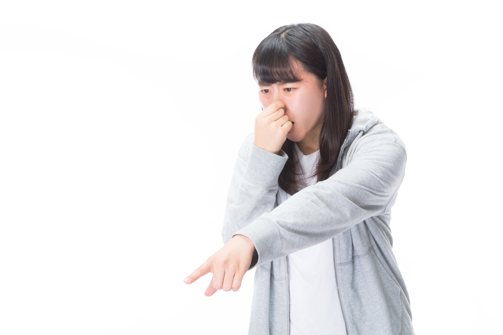 鼻をつまんで指をさしながら嫌がる表情の白い服を着た女性［モデル：Mizuho］