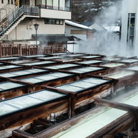 ズラリと並ぶ木の樋から湯けむりが立ち上る草津温泉湯畑の写真