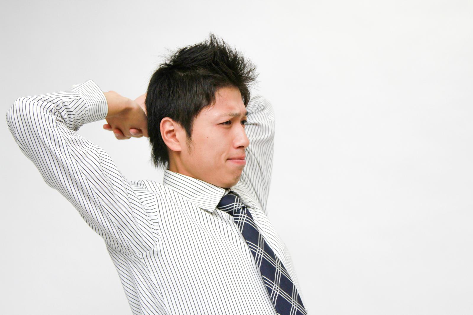 ネクタイをした男性が両腕を上げて背伸びしている［モデル：恭平］
