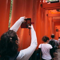 朱塗り千本鳥居でスマホ撮影する白い服の外国人観光客・伏見稲荷大社の写真