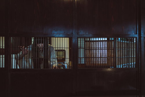 古民家の格子戸の隙間越しに暗闇を覗き見る女性