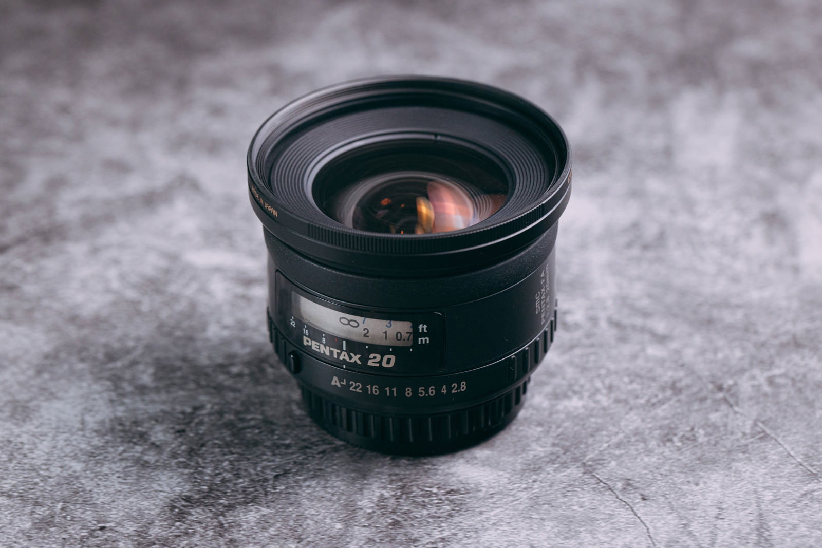 グレーの表面に置かれたPentax-FA 20mm F2.8の黒い広角レンズ