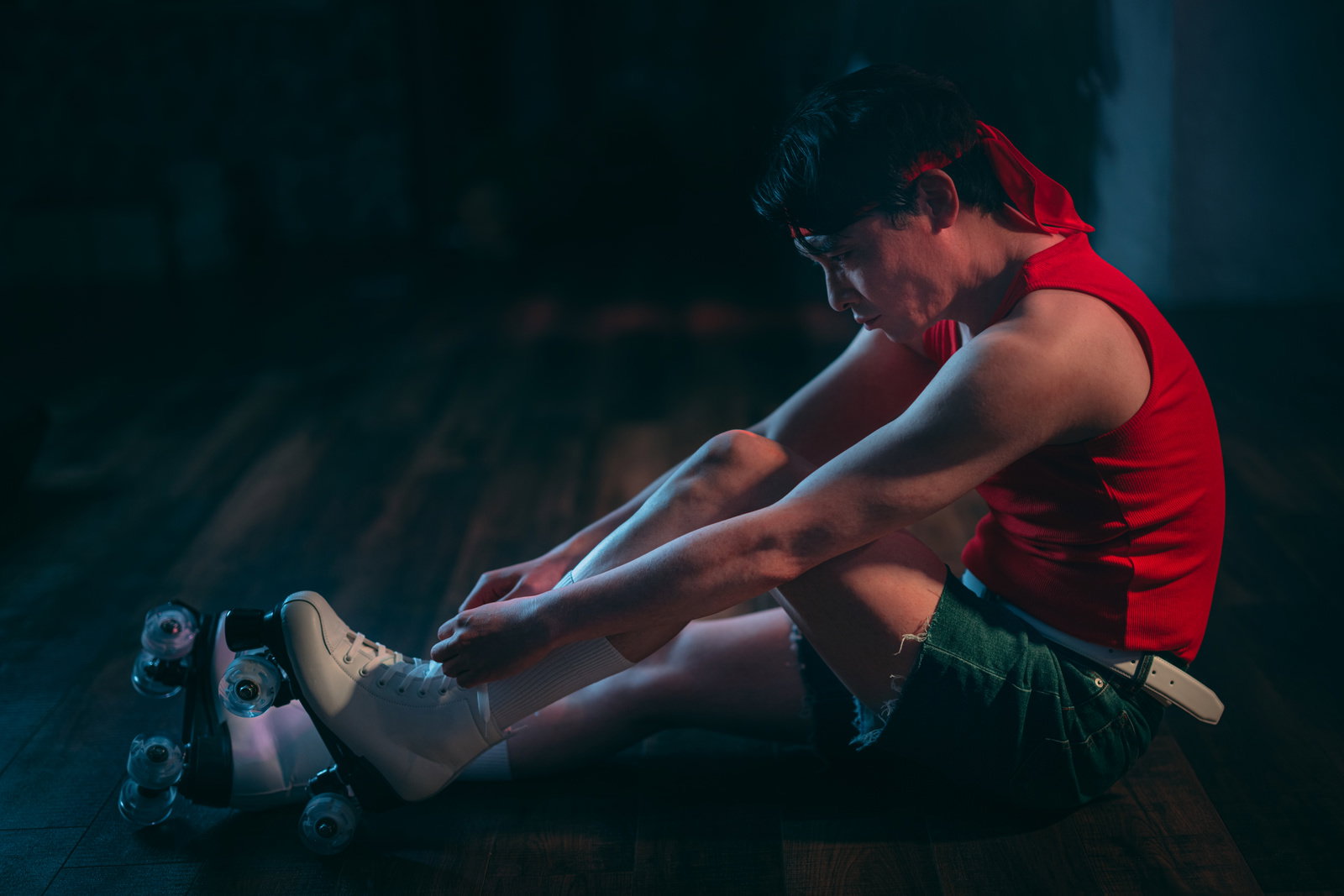 赤いベストを着たアイドル男性がローラースケート靴を調整しながら座っている［モデル：金子周平］