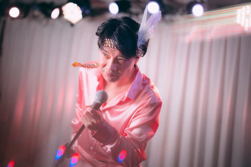 ステージ上で熱唱する男性アイドル、ピンク照明の中でマイクを握る