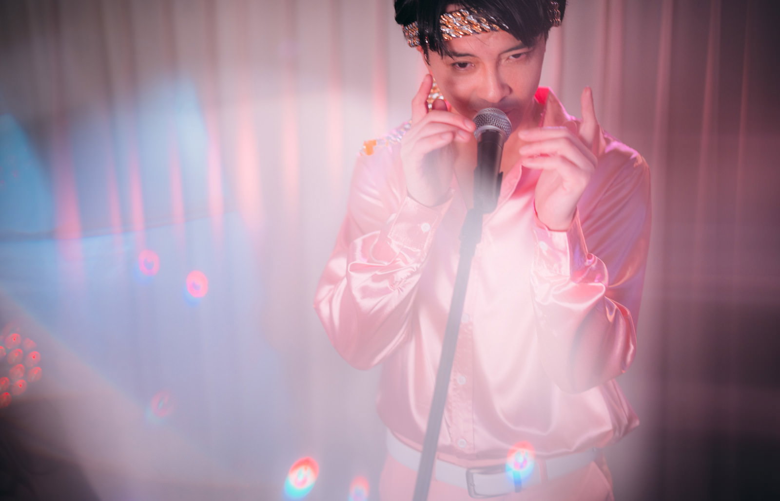 ピンク色のジャケットを着た男性がマイクを握りながらステージで熱唱している［モデル：金子周平］