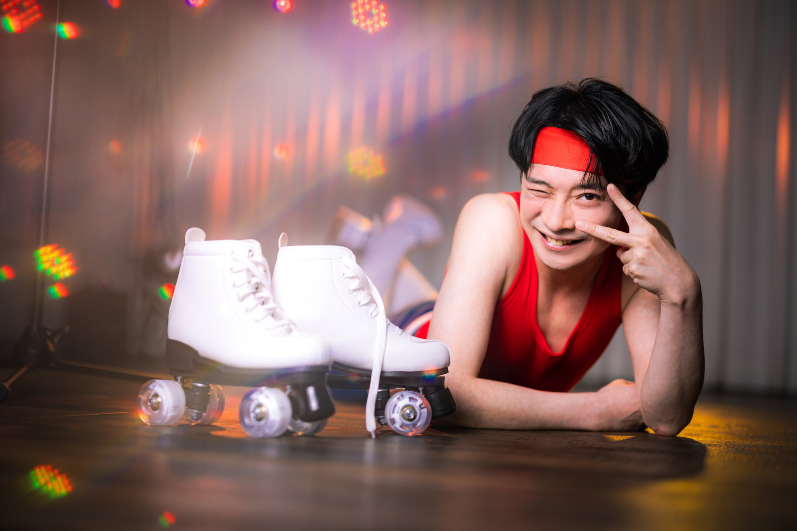 赤いヘッドバンドを着けた男性がローラースケートに乗ってピースをしながら笑顔でステージに立つ［モデル：金子周平］