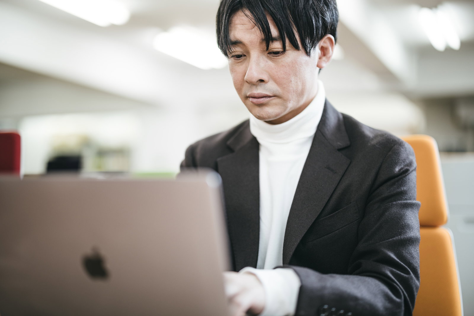 スーツ姿の男性がオフィスでMacBookを操作［モデル：金子周平］