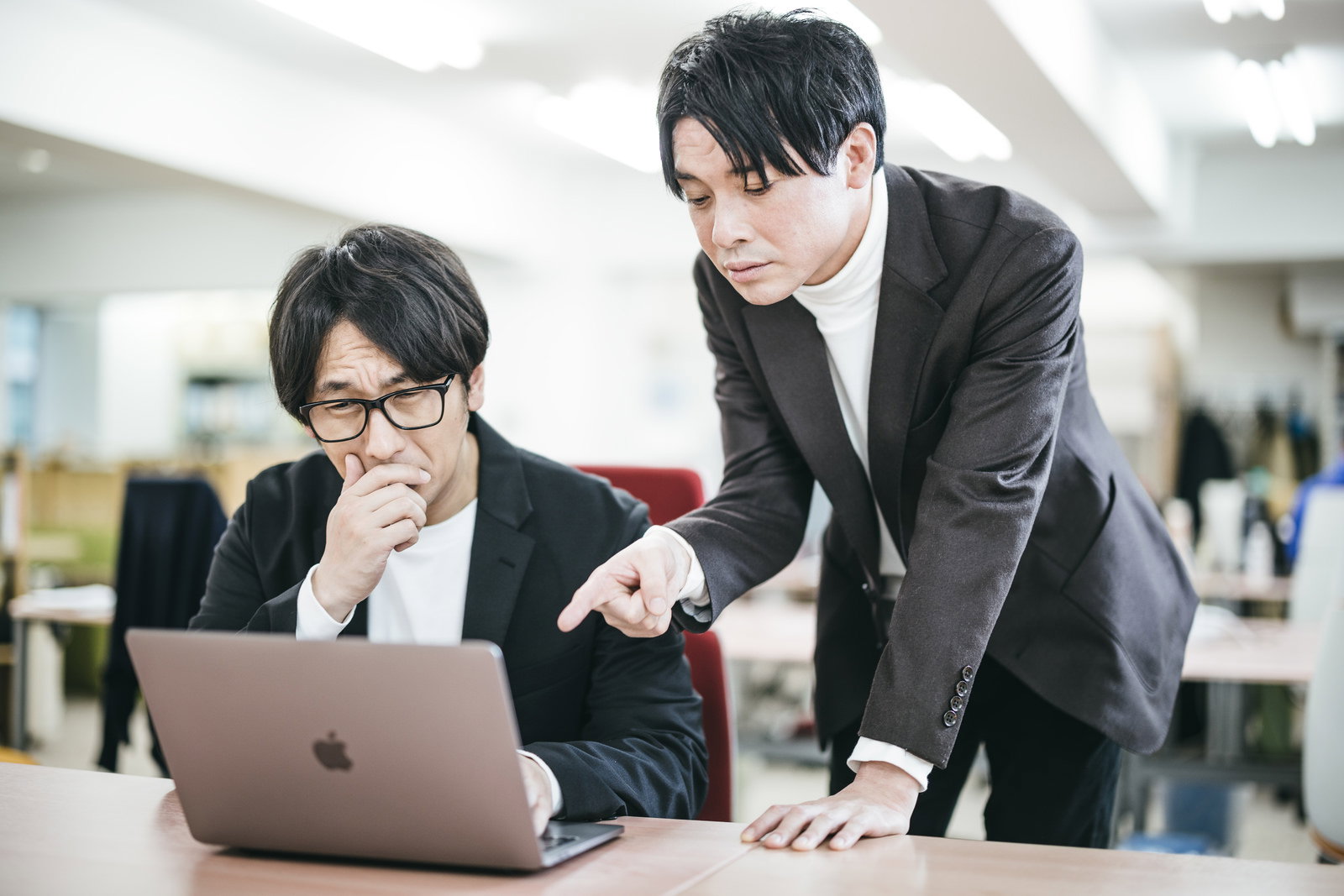 パソコン画面を指しながら部下に指摘する眼鏡の男性上司［モデル：大川竜弥 金子周平］