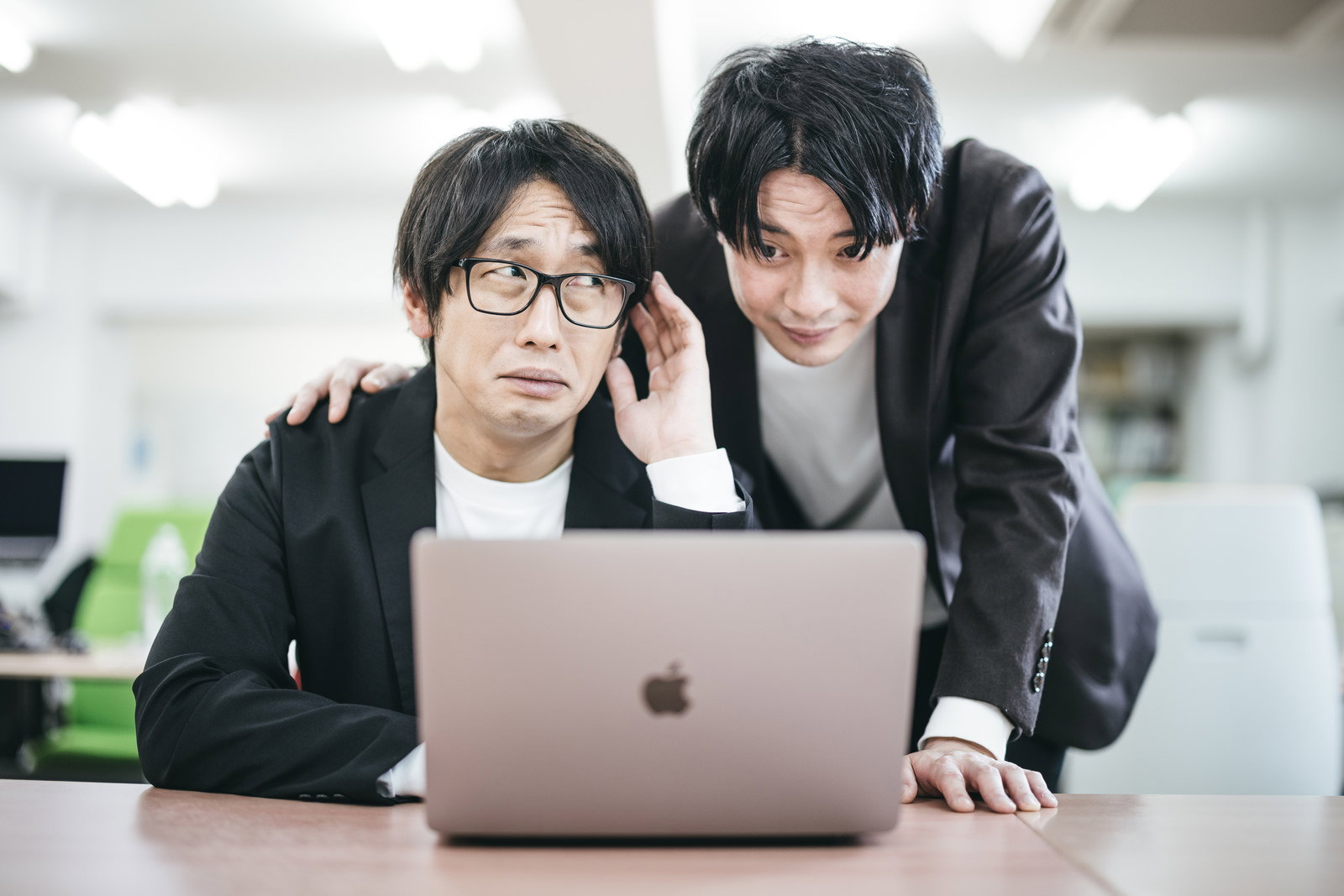 オフィスでノートパソコンを見つめる男性社員に、眼鏡の上司が肩に手を置き話しかけている［モデル：金子周平］
