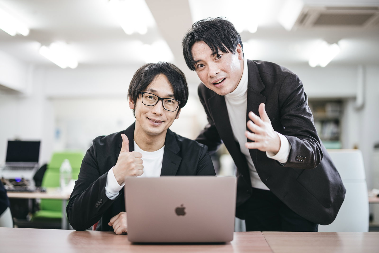 オフィスでMacBookを前にポーズをとる男性2人［モデル：金子周平］