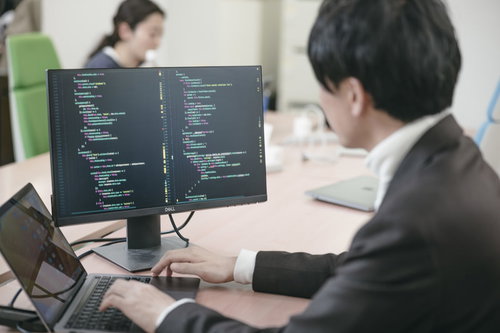 サブモニターのコード画面を見るエンジニア男性