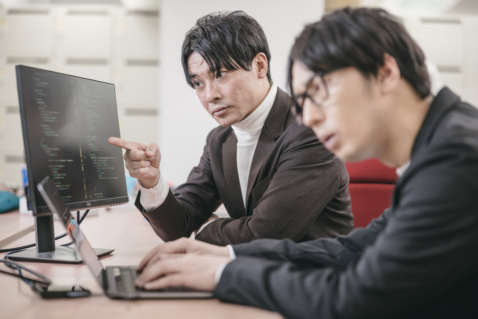 モニターのコードを指して説明する男性と、話を聞く男性社員［モデル：大川竜弥 金子周平］