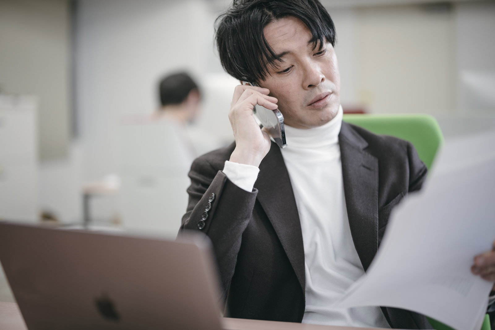 電話で指示を出すビジネス役員。ノートパソコンを見ながら通話する男性［モデル：金子周平］