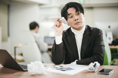 紙の書類に飽き飽きして紙ヒコーキを飛ばしはじめる役員男性