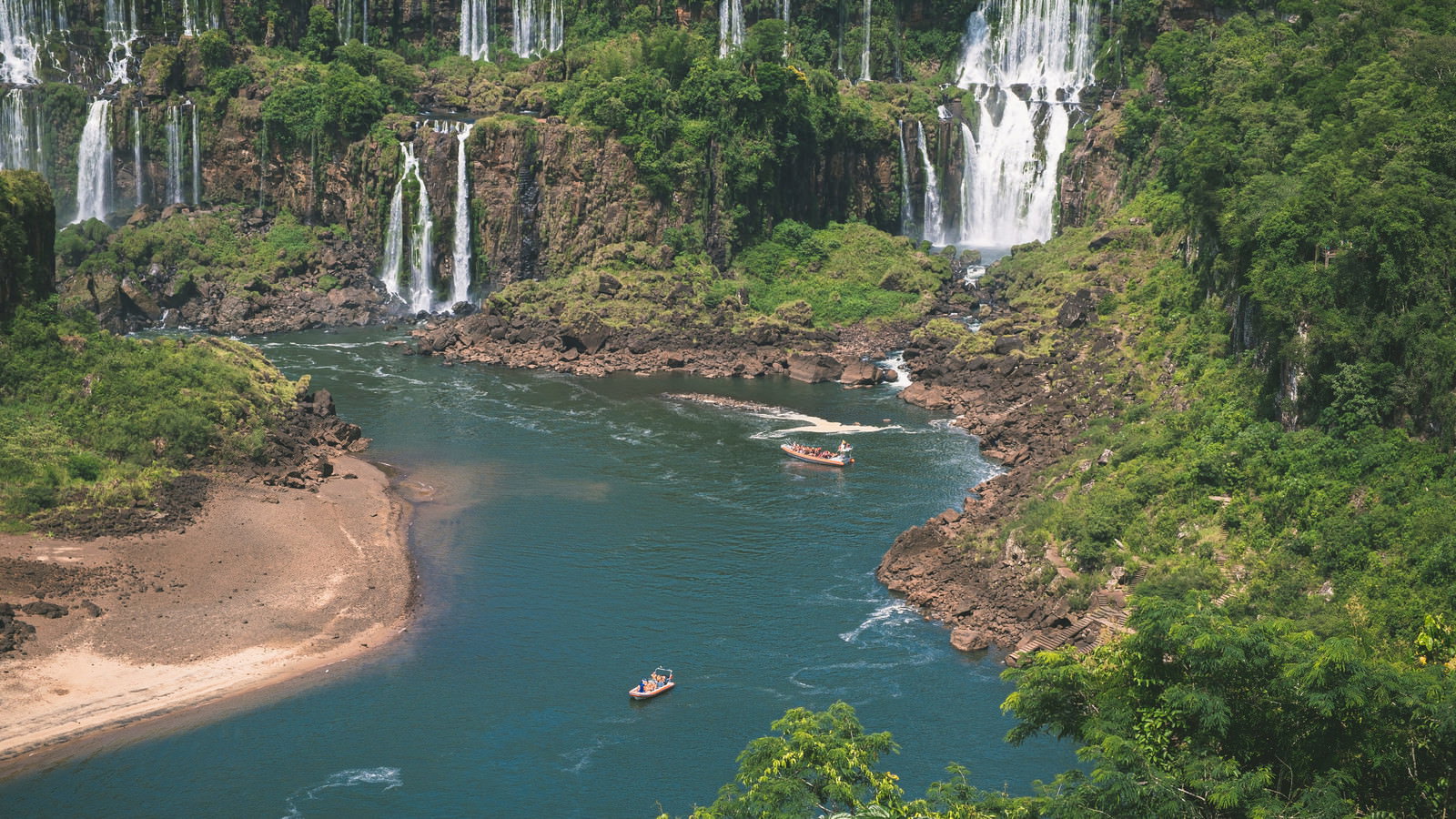 イグアス川のエメラルドグリーンの水面を進む赤いツアーボート