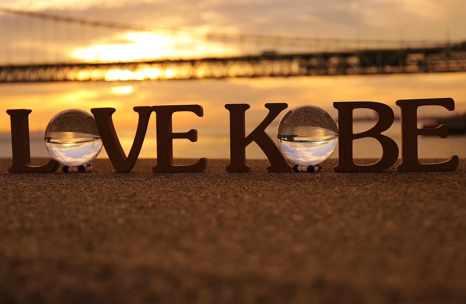 夕日の海辺でLOVE KOBEの文字と透明なガラス玉が置かれている