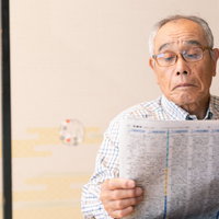 眼鏡をかけて新聞を読む高齢男性の室内での読書風景の写真