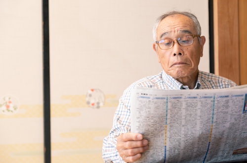 眼鏡をかけて新聞を読む高齢男性の室内での読書風景