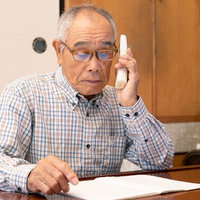 机の書類を見ながら電話をするオレオレ詐欺の高齢男性の写真