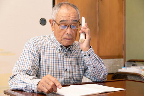 机の書類を見ながら電話をするオレオレ詐欺の高齢男性