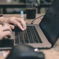 木目のデスクで作業中のMacBookとスマートウォッチの写真