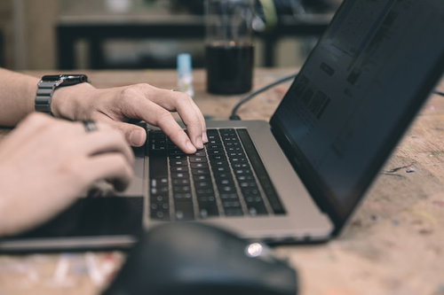 木目のデスクで作業中のMacBookとスマートウォッチ